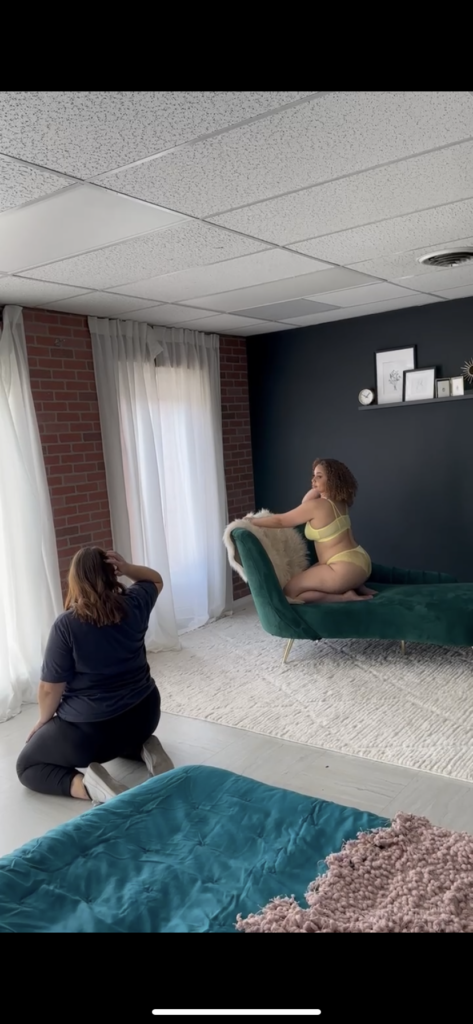 boudoir photographer is showing posing direction to poc client on couch in boudoir studio in kansas city