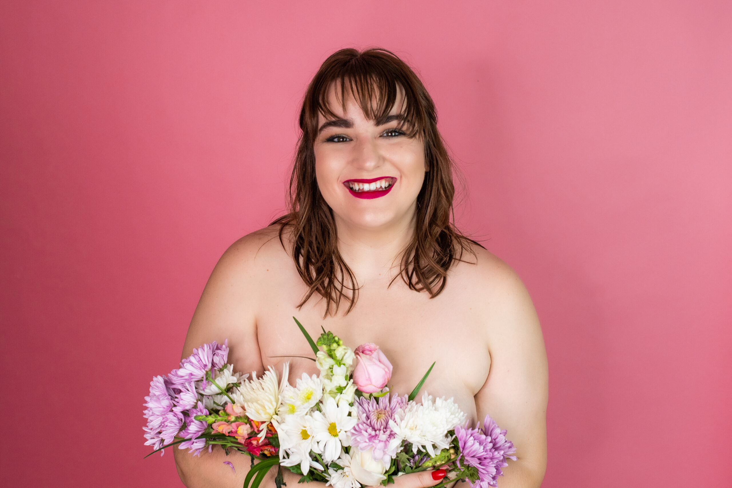 plus size woman holds flowers in front of pink backdrop in kansas city boudoir studio